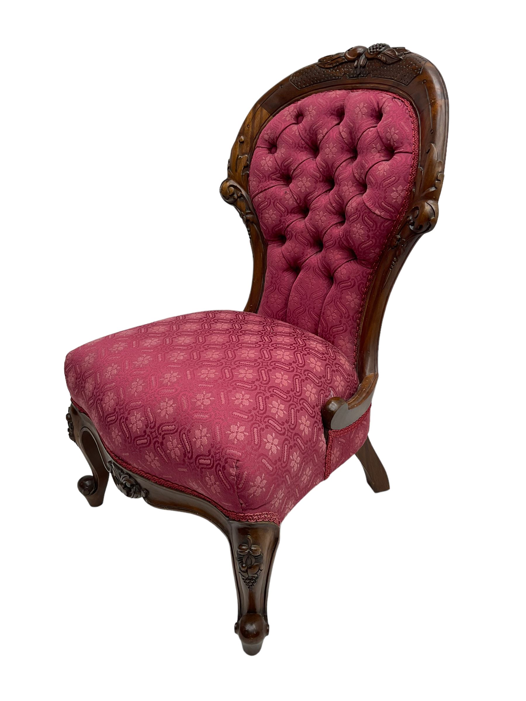 Victorian style mahogany framed nursing chair, the cresting rail carved with fruit and foliage, upholstered in red patterned fabric with buttoned back, on cabriole supports with scrolled terminals