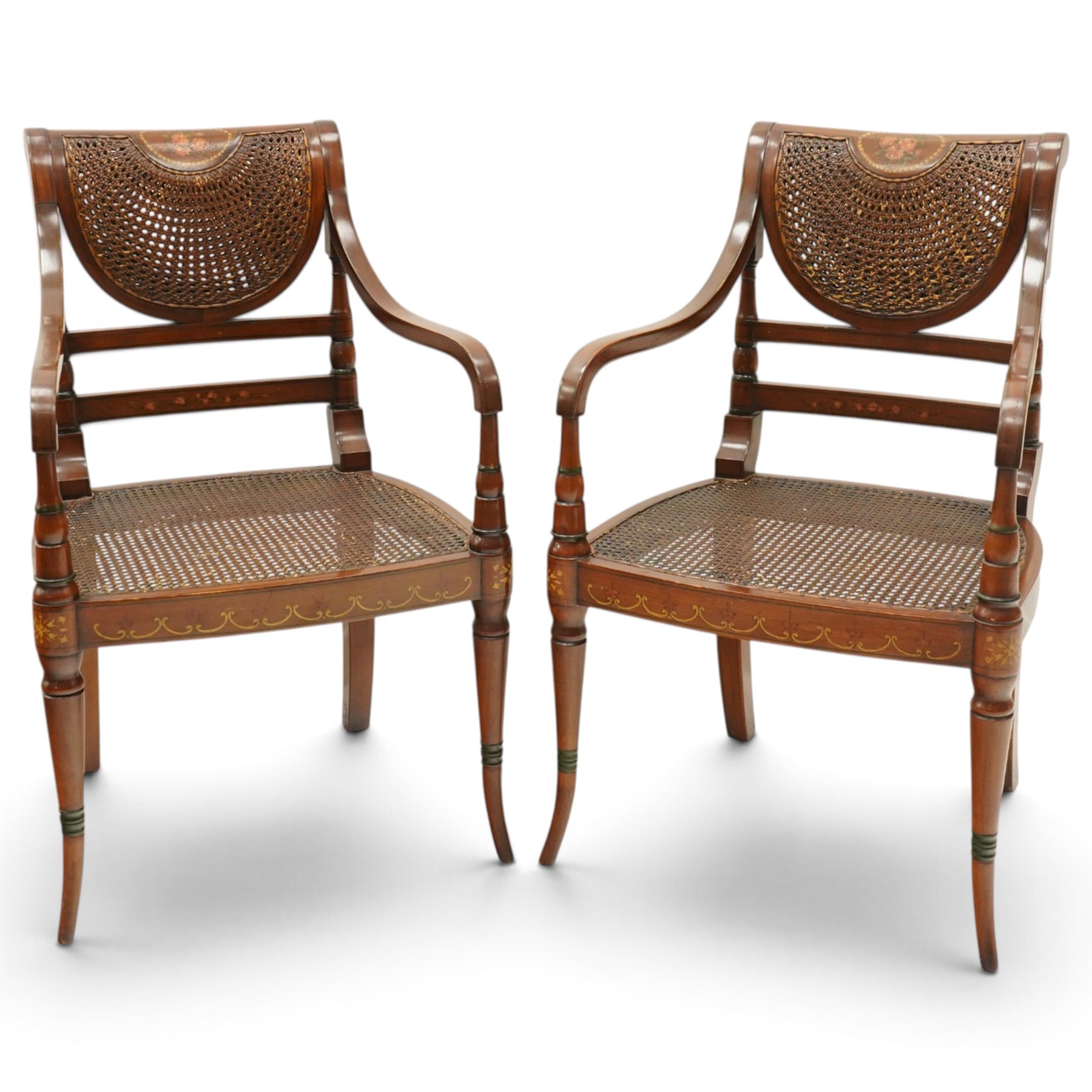 Pair of Sheraton Revival painted mahogany open armchairs, scrolled cresting rail with floral painted decoration over a double-caned back and rose-branch painted back bar, cane seat over C-scroll-painted seat rail, on splayed tapering supports, with all-over painted ebony faux stringing
