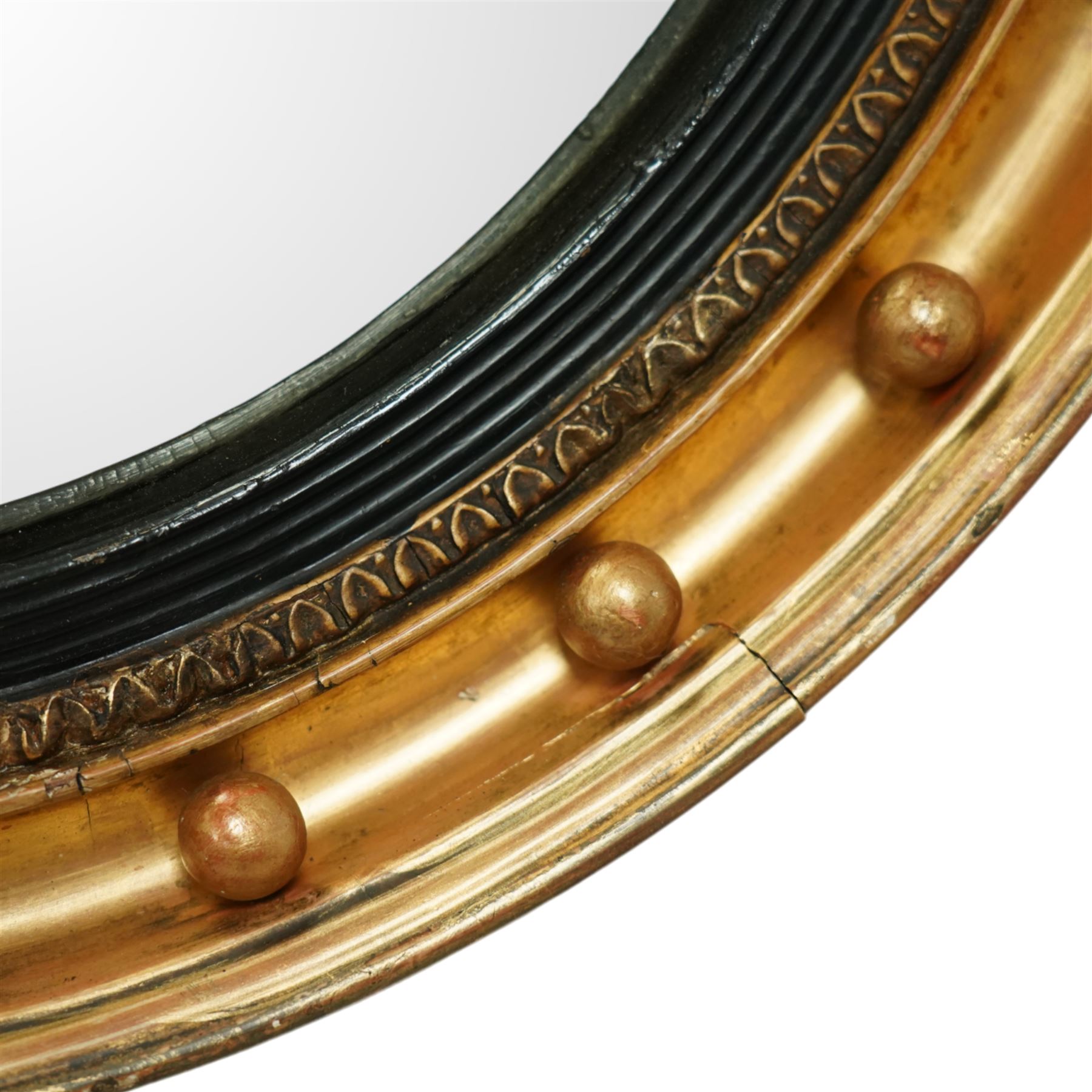 Regency period eagle mounted giltwood convex mirror, surmounted by a finely carved giltwood eagle standing on rocks above the circular mirror with the original mirror plate and surrounded by a fluted ebonized slip and the convex frame with gilt ball decorations, the back with label for ‘T.G. Woof Ltd, manufacturing cabinet makers, Devonshire Street, Sheffield