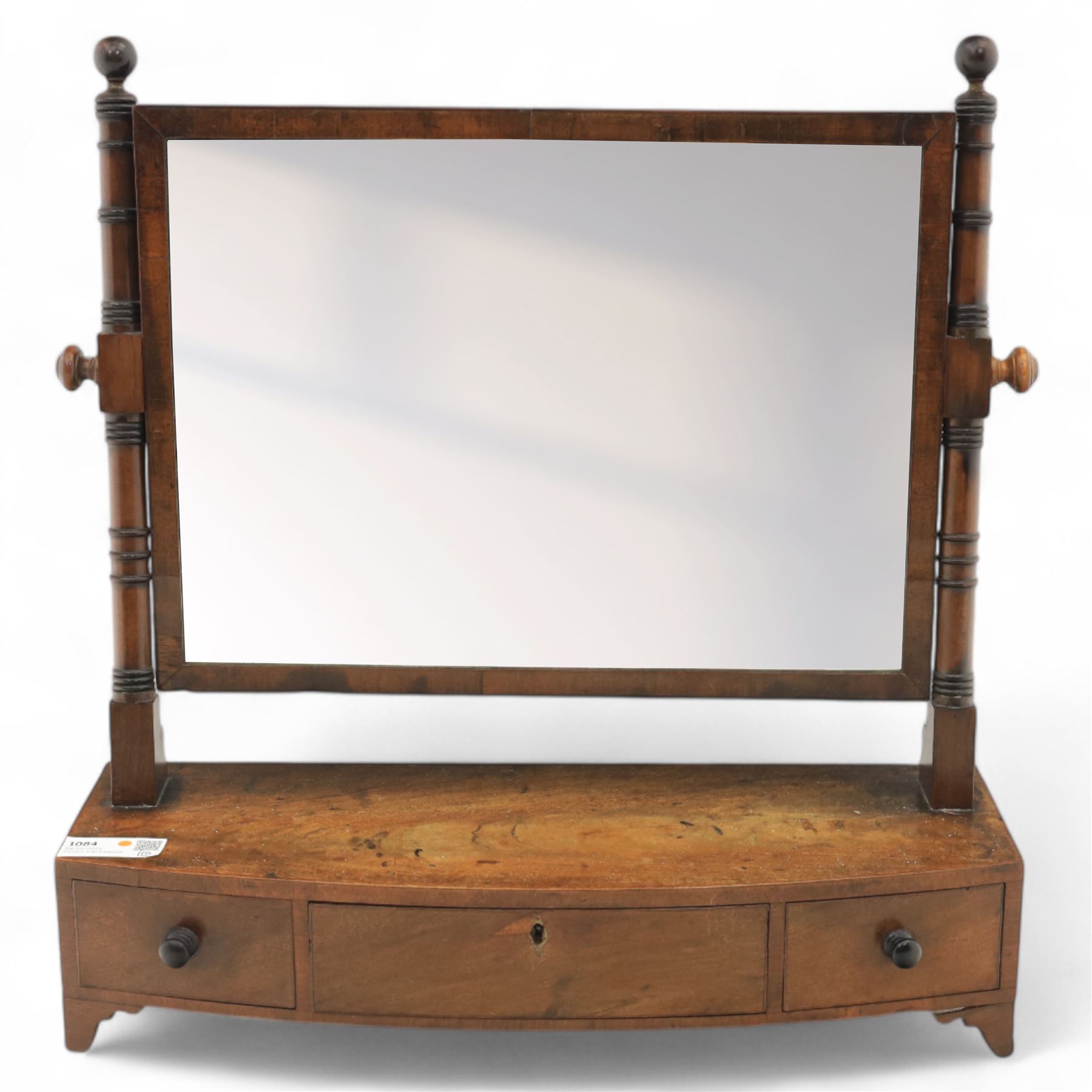19th century mahogany swing mirror, rectangular frame on turned supports with ball finials, bow front base fitted with three drawers and ebony knob handles, raised on shaped feet