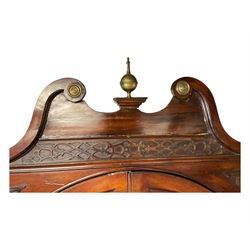 George III mahogany corner cabinet, the scrolled pediment surmounted by a brass finial and carved fretwork frieze, with fluted uprights flanking arched double doors over a painted interior fitted with shaped shelves, above a lower cupboard with twin panelled doors, on plinth base