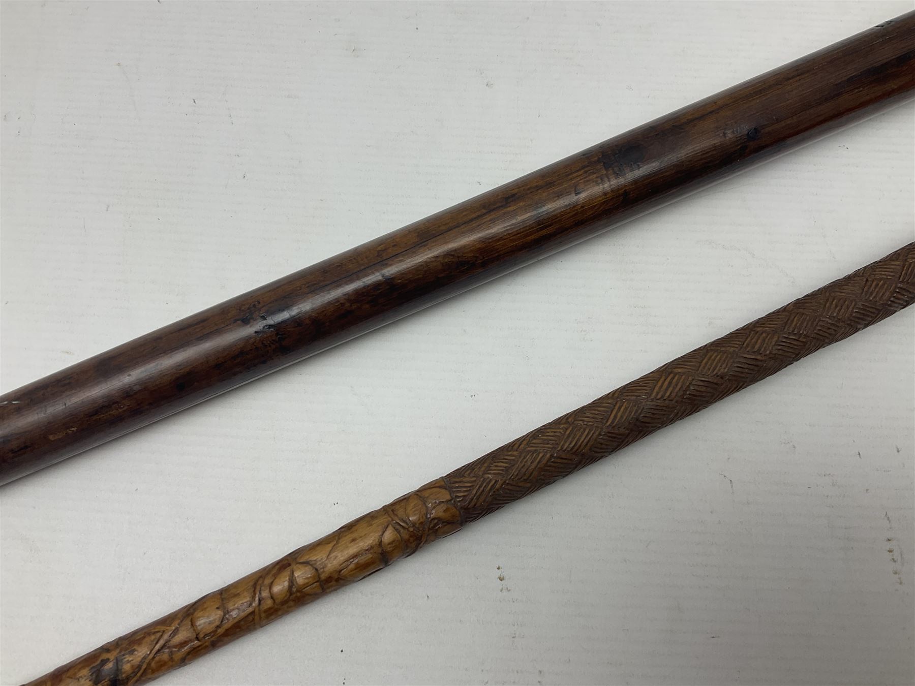 19th century wooden walking stick, the handle carved as a snake within a clenched fist, the cane carved with foliate and cross hatched decoration, with a metal spike to base, together with a turned wooden walking stick, with lacquered rope nautical knot handle, tallest L96.5cm