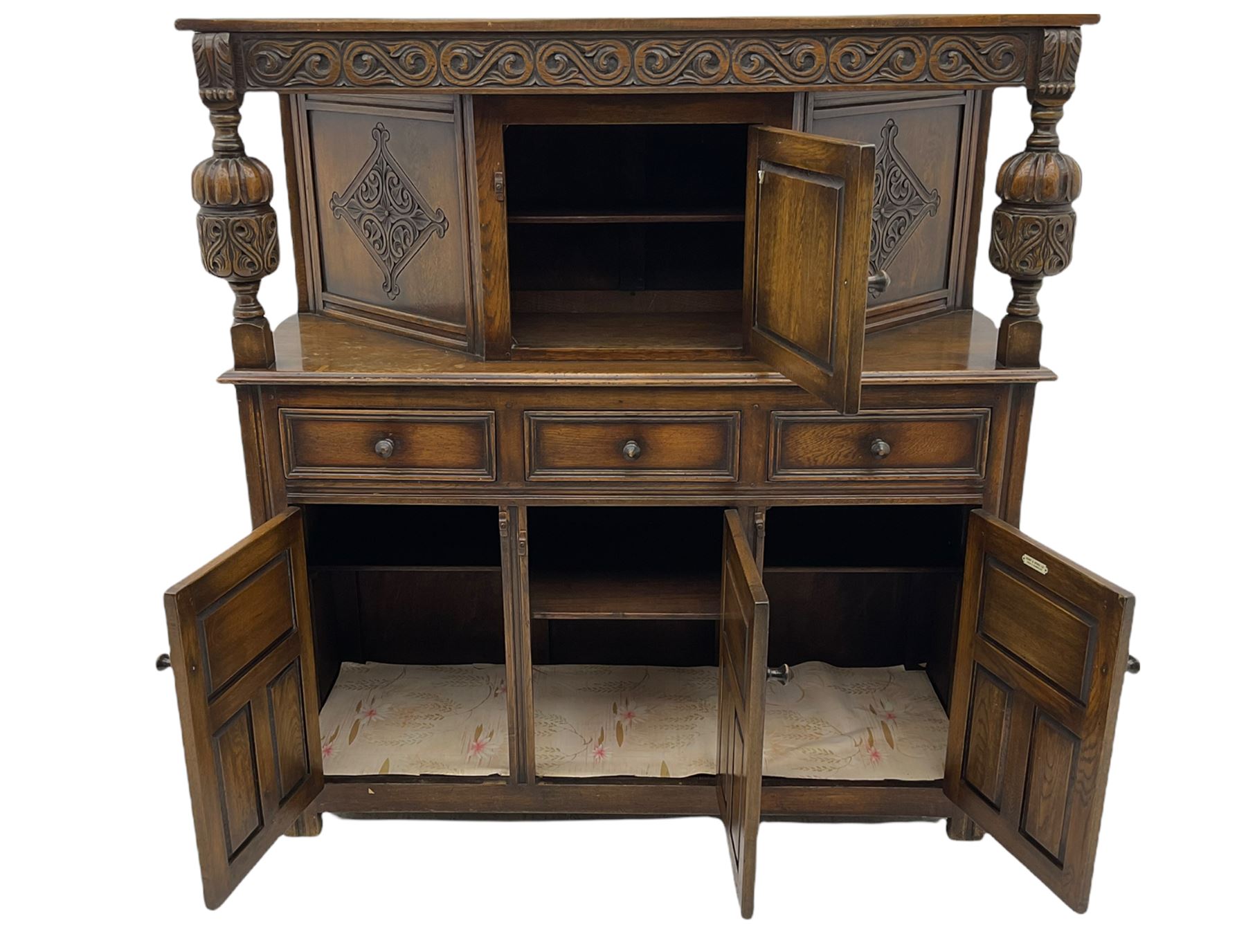 20th century carved oak court cupboard, s-scroll carved frieze over panelled cupboard door carved with arch, lobe and scroll carved cup and cover supports, fitted with three drawers and three cupboards below
