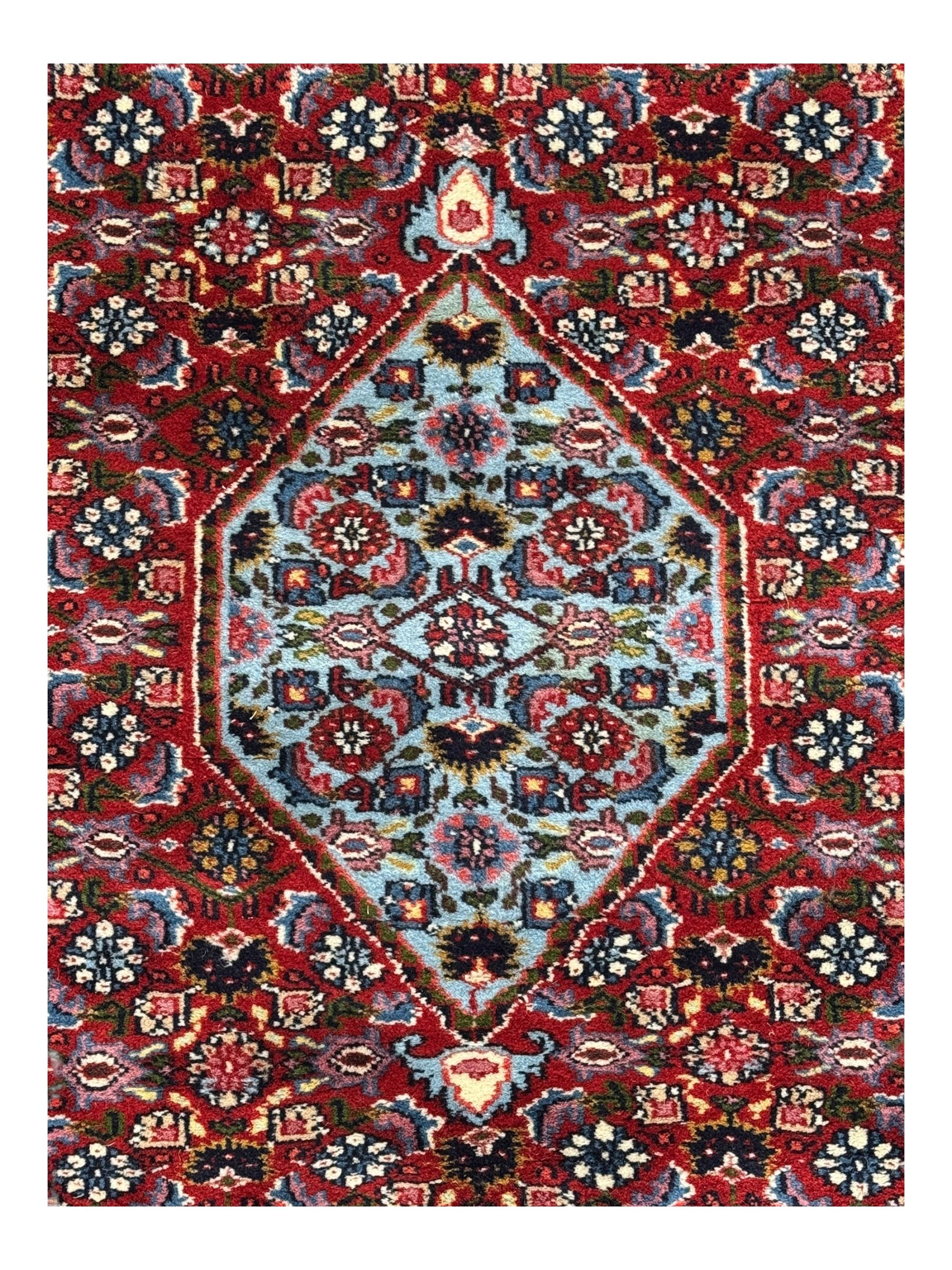 Persian crimson ground rug, central light blue lozenge medallion with floral motifs, the densely decorated crimson field filled with repeating flower heads and trailing leafy vines, the black and red border with interlacing foliate patterns and floral cartouches, surrounded by guard stripes