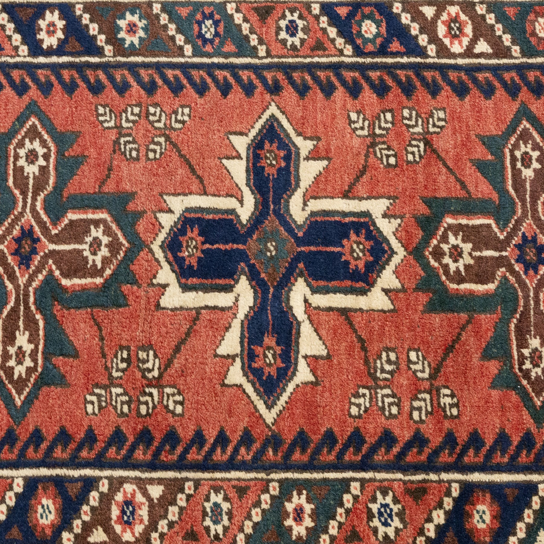 Caucasian Kazak rug, red field with three bold geometric medallions in dark blue, cream and brown, scattered tribal motifs, broad indigo border decorated with stylised hooked forms and multiple narrow patterned borders