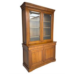 French cherry wood bookcase on cupboard, projecting cornice over two cupboard doors with bevelled glass panels enclosing three adjustable shelves, base fitted with two cushion drawers over double cupboard