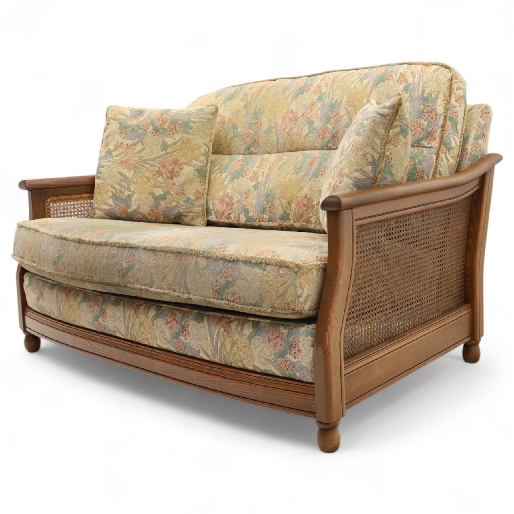 Ercol – bergère four piece suite, including armchair, two seat sofa, three seat sofa and footstool, all with removable floral upholstered cushions, the frames with side caning and rounded arm supports in stained beech

Three seat (H 87cm, D 89cm, W 196cm)
Two seat (H 87cm, D 89cm, W 137cm)
Armchair (H 87cm, D 89cm, W 87cm)
Footstool (H 28cm, D 55cm, W 55cm)
