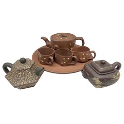 Three Chinese Yixing clay teapots, the first example with marbled decoration, the second with mountainous river landscape with figures and huts amongst trees, both with impressed character seal marks, and further with irregularly shaped body moulded in relief with blossoming branches, with three matching teacups housed on a dish, dish D24cm (7)