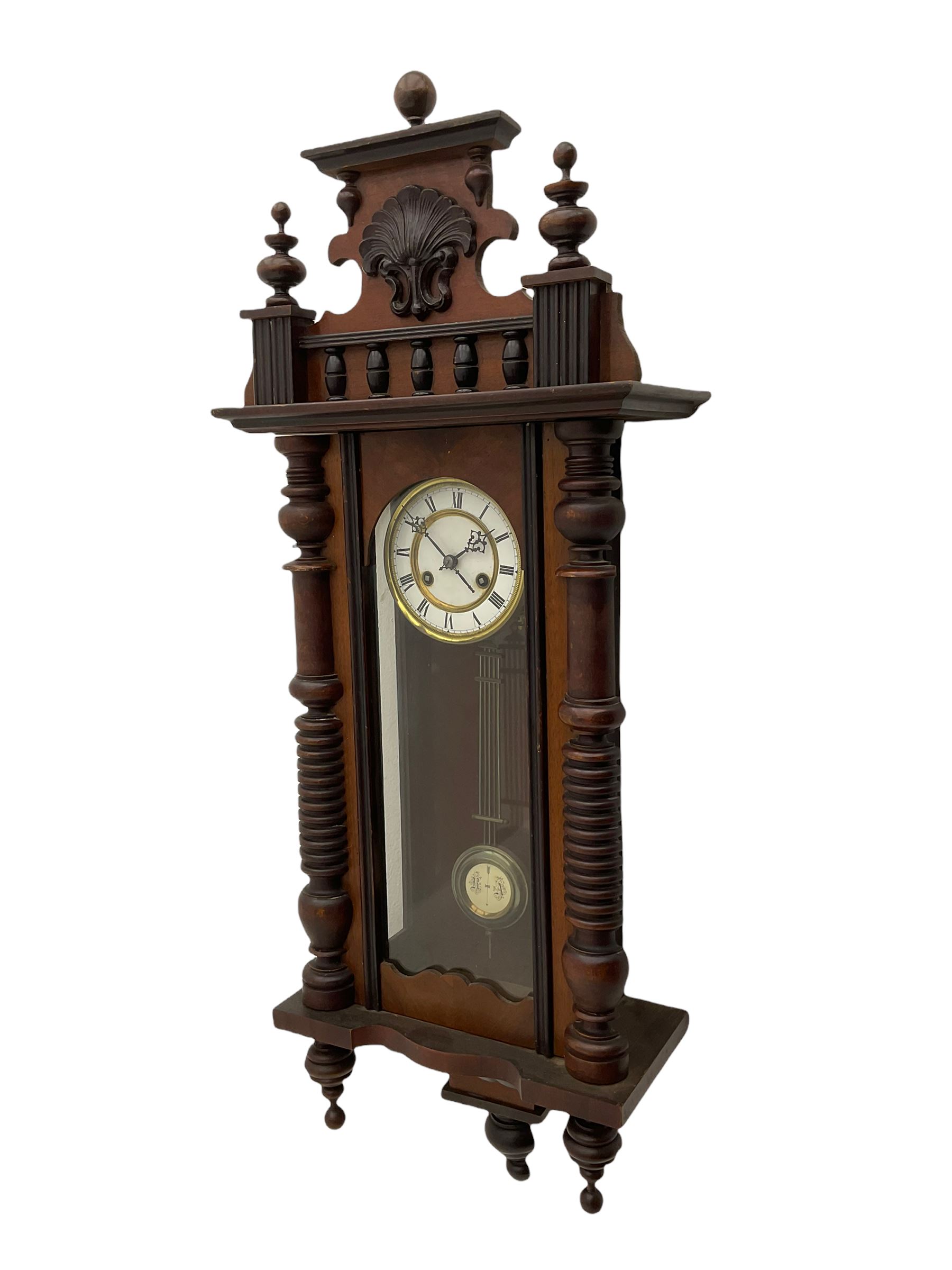 A  German spring driven wall clock c1900 within a glazed case with side panels and a full-length arched door and ornately carved pediment, turned finials and original pendant finials, with a 5' two-piece white enamel dial with roman numerals, minute markers and pierced steel gothic hands, with a visible gridiron pendulum with an R/A inscribed pressed brass bob, eight-day movement striking the hours and half hours on a coiled gong.  




