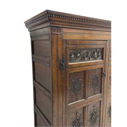 Large 18th century and later oak livery cupboard, projecting moulded and dentil cornice, sunken fillet moulded frame, triple vertical panelled central upright, enclosed by two doors each with five panels, the top row of panels carved with stylised scrolls, the lower panels carved with foliate lozenges, on shaped bracketed skirt base 