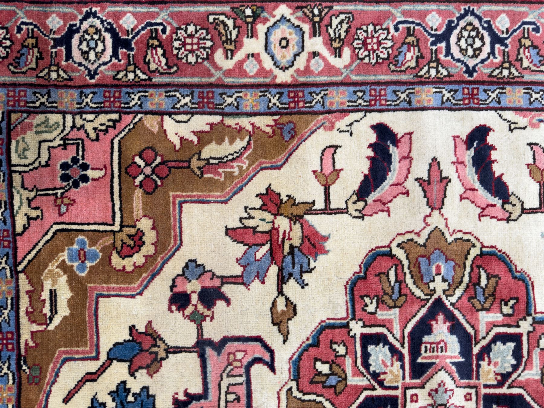 Northwestern Persian Heriz hand-knotted rug,  ivory field with a bold stepped medallion in madder red, navy and pale blue, surrounded by angular floral motifs and stylized leaves, the spandrels in camel and rose with a madder-red border of rosettes and angular vine motifs between multiple guard stripes, 180cm x 156cm