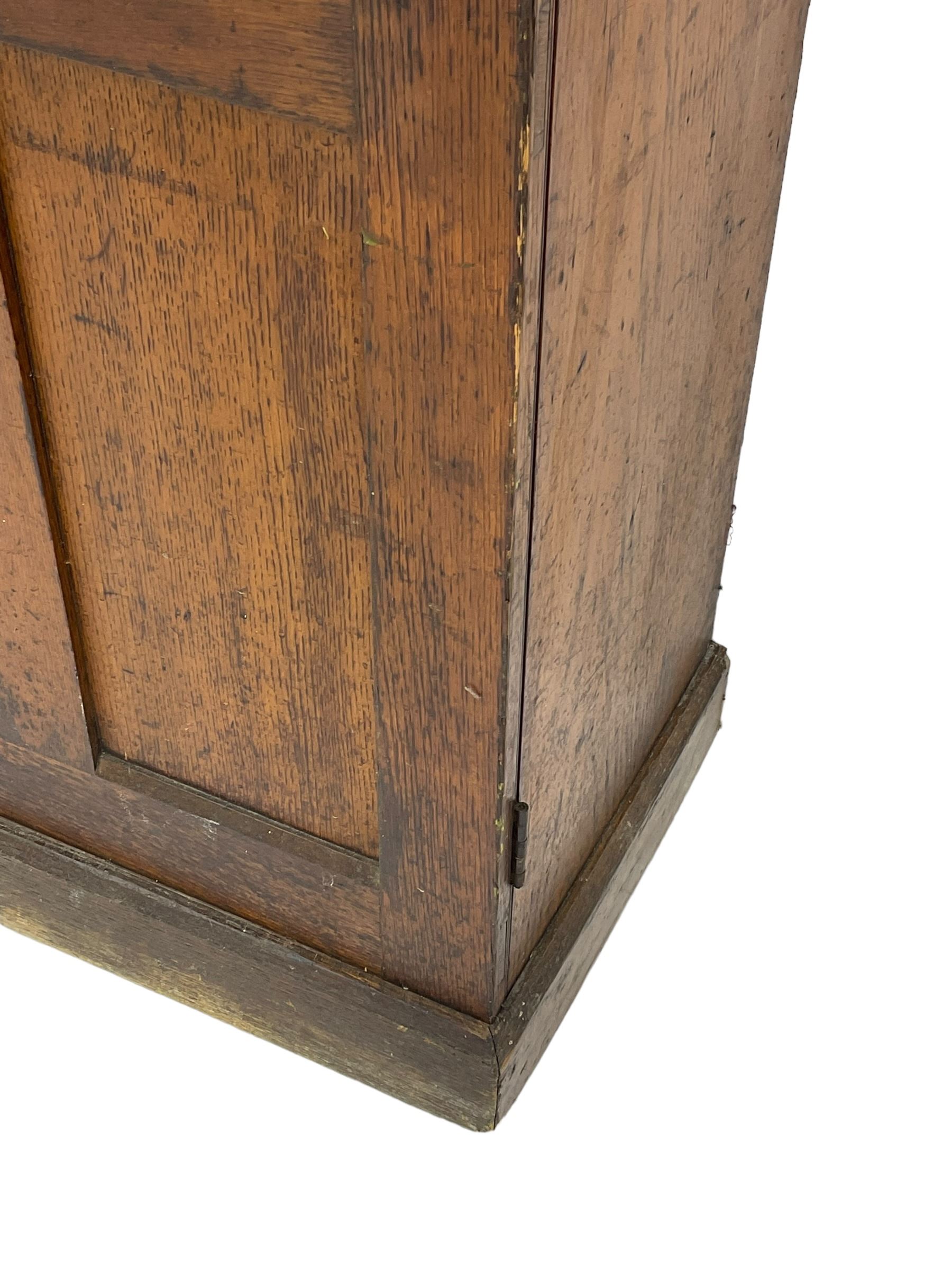 The North of England School Furnishing Company Limited Darlington - early 20th century oak school cupboard, projecting moulded cornice over two panelled doors, fitted with shelves, on chamfered plinth base 