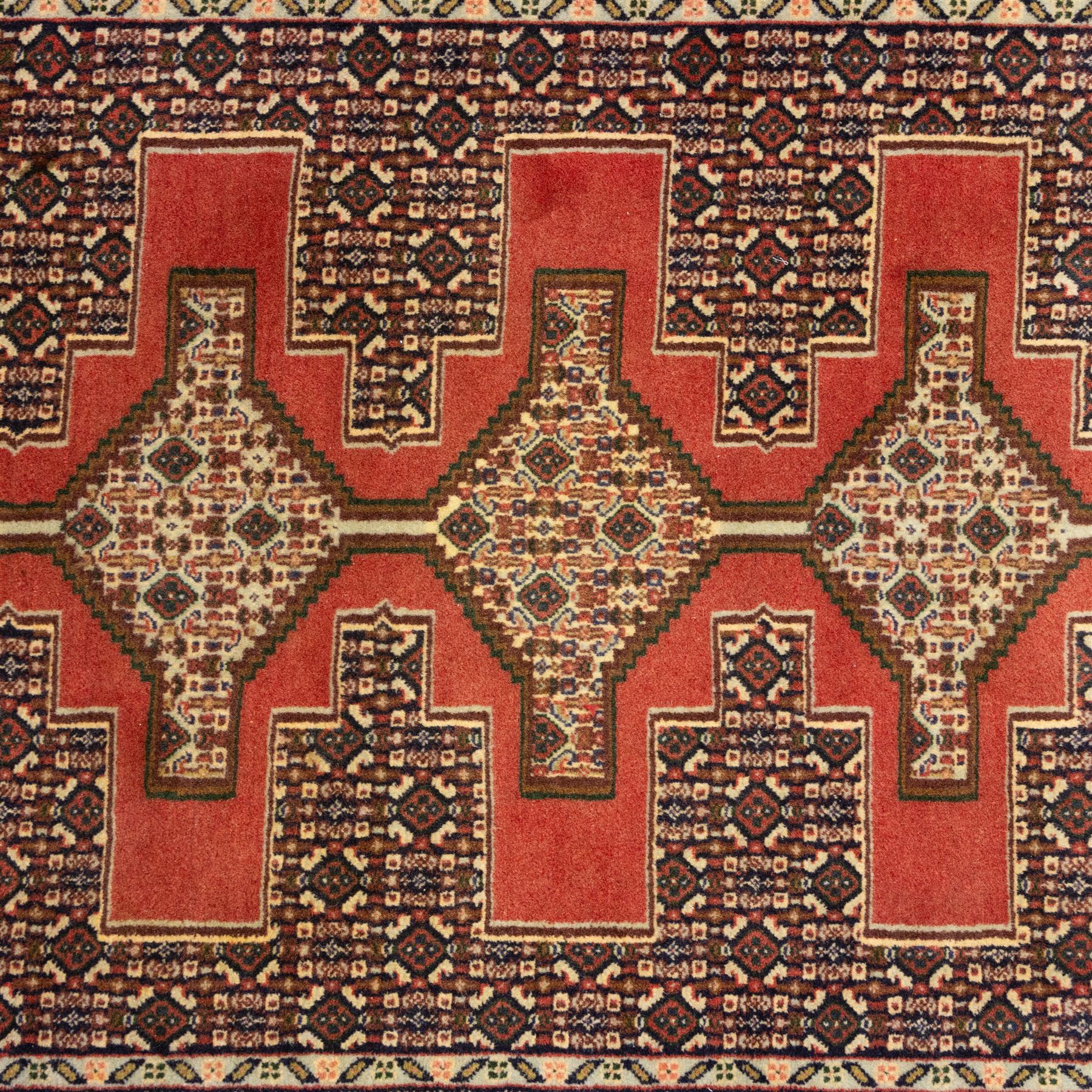 North West Persian Senneh hand-knotted runner, decorated with a continuous series of stepped and hooked geometric medallions against a madder red ground, enclosing herati style and small geometric floral motifs, framed by a principal border and flanked by multiple narrow guard stripes, with cotton fringe ends 
