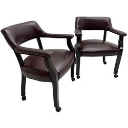 Pair of tub shaped armchairs, upholstered in burgundy faux leather with studwork, raised on square supports with castors