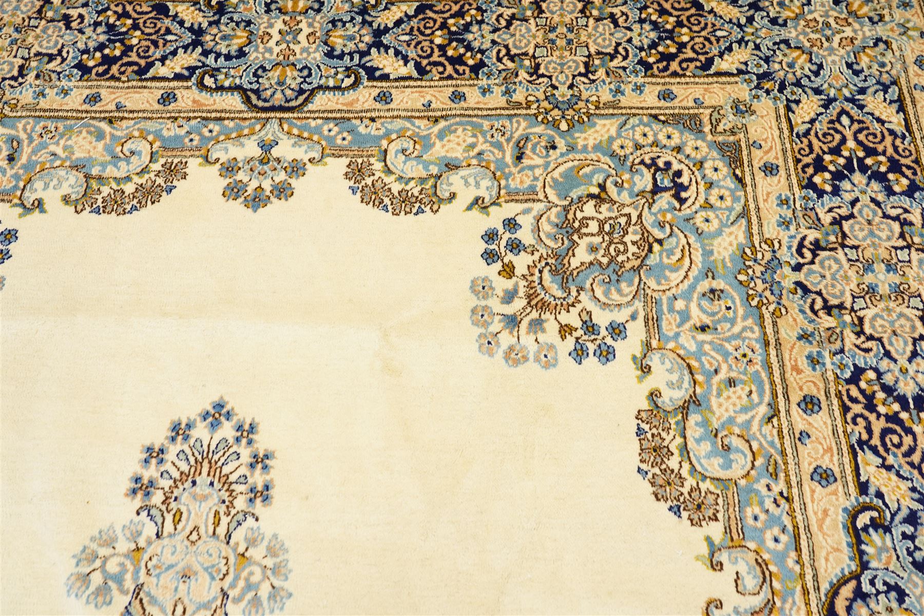 South East Persian Kirman hand-knotted carpet, ivory field with central floral medallion in tones of cobalt and pale blue, issuing scrolling vinery and palmettes, conforming spandrels, main border with scrolling foliage and stylized palmettes, framed by multiple guard borders, with cotton fringe ends 