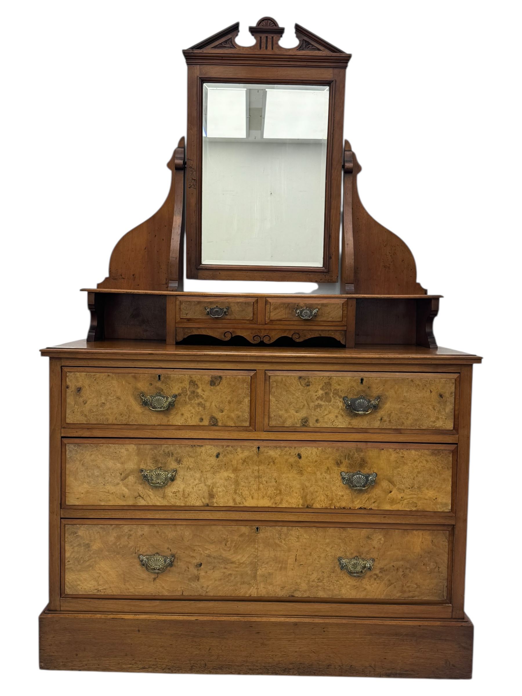 Victorian walnut bedroom suite - wardrobe, dressing chest and bedside cupboard, comprising a full-length wardrobe with broken pediment and central mirrored door, large lower drawer, a matching dressing table with bevelled swing mirror over two trinket drawers and two short drawers over two long drawers, and a single-door bedside cupboard, all with moulded edges, decorative panel work and shaped aprons