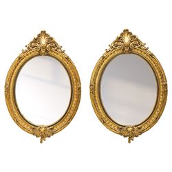 Pair of Rococo Revival gilt framed oval wall mirrors, the exuberant pediment formed of scr...