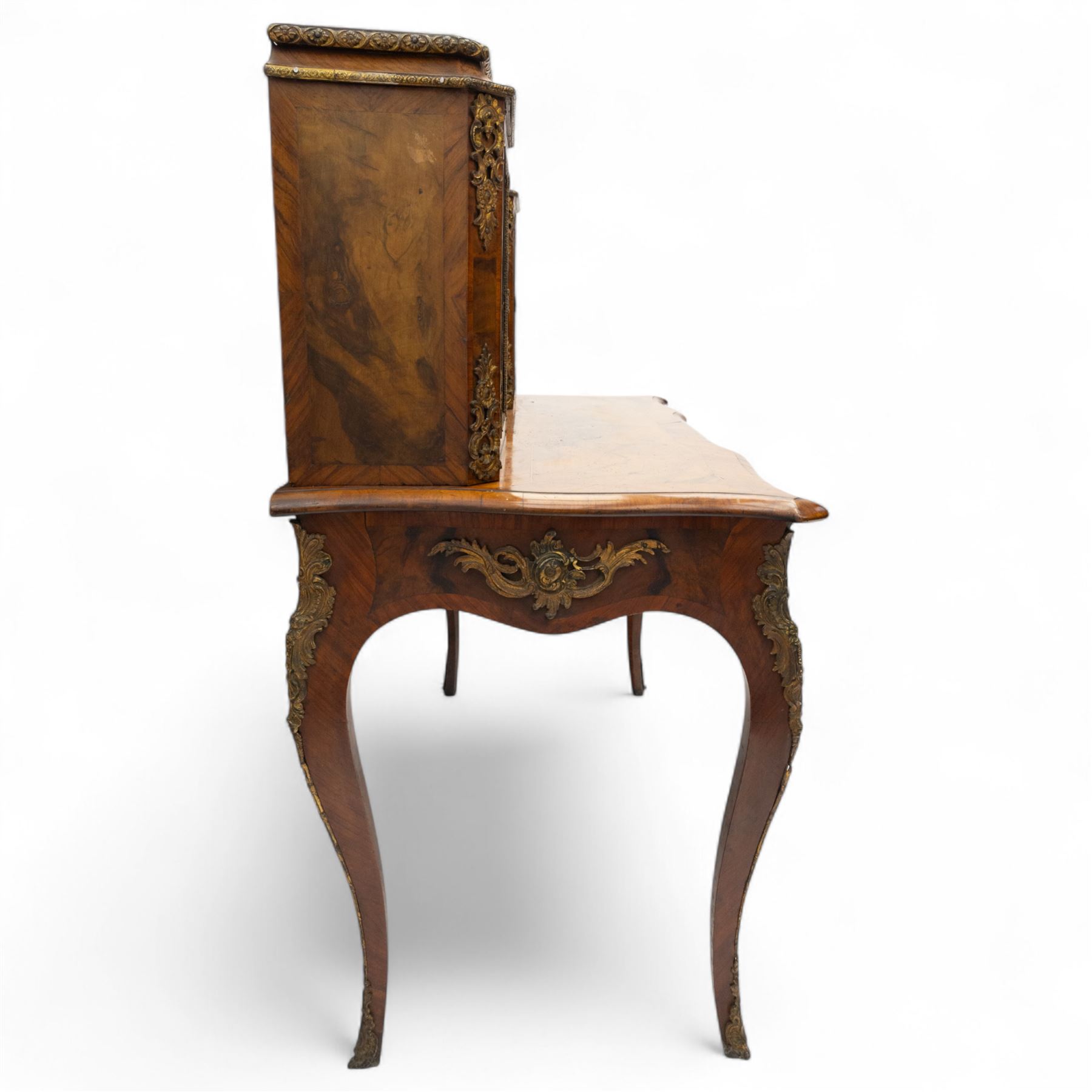 Late 19th-century Louis XV revival gilt bronze mounted and walnut Bonheur-de-Jour, rectangular-shaped serpentine form, with gilt bronze beading, frieze with two blind drawers and gilt bronze handles, centre drawer with large central serves style porcelain plaque, the elevated section with brass gallery above panelled cupboard doors also with serves style porcelain plaques and gilt bronze mounts, interior with single shelf, central section with four drawers each with gilt bronze handles, raised on slender cabriole legs fitted with gilt bronze rococo style masks and sabots