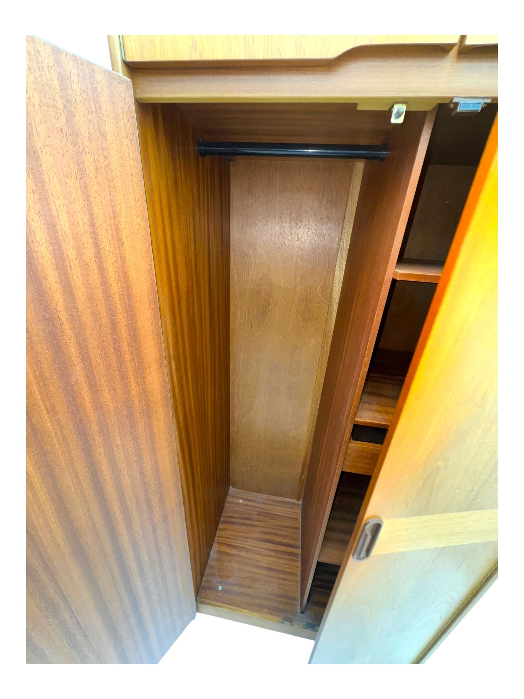 William Lawrence - mid-20th century teak double wardrobe, upper storage section over twin doors featuring recessed handles and contrasting horizontal panel, enclosing hanging rail compartment, towel rail, mirror, shelves and drawer, on plinth base with concealed castors