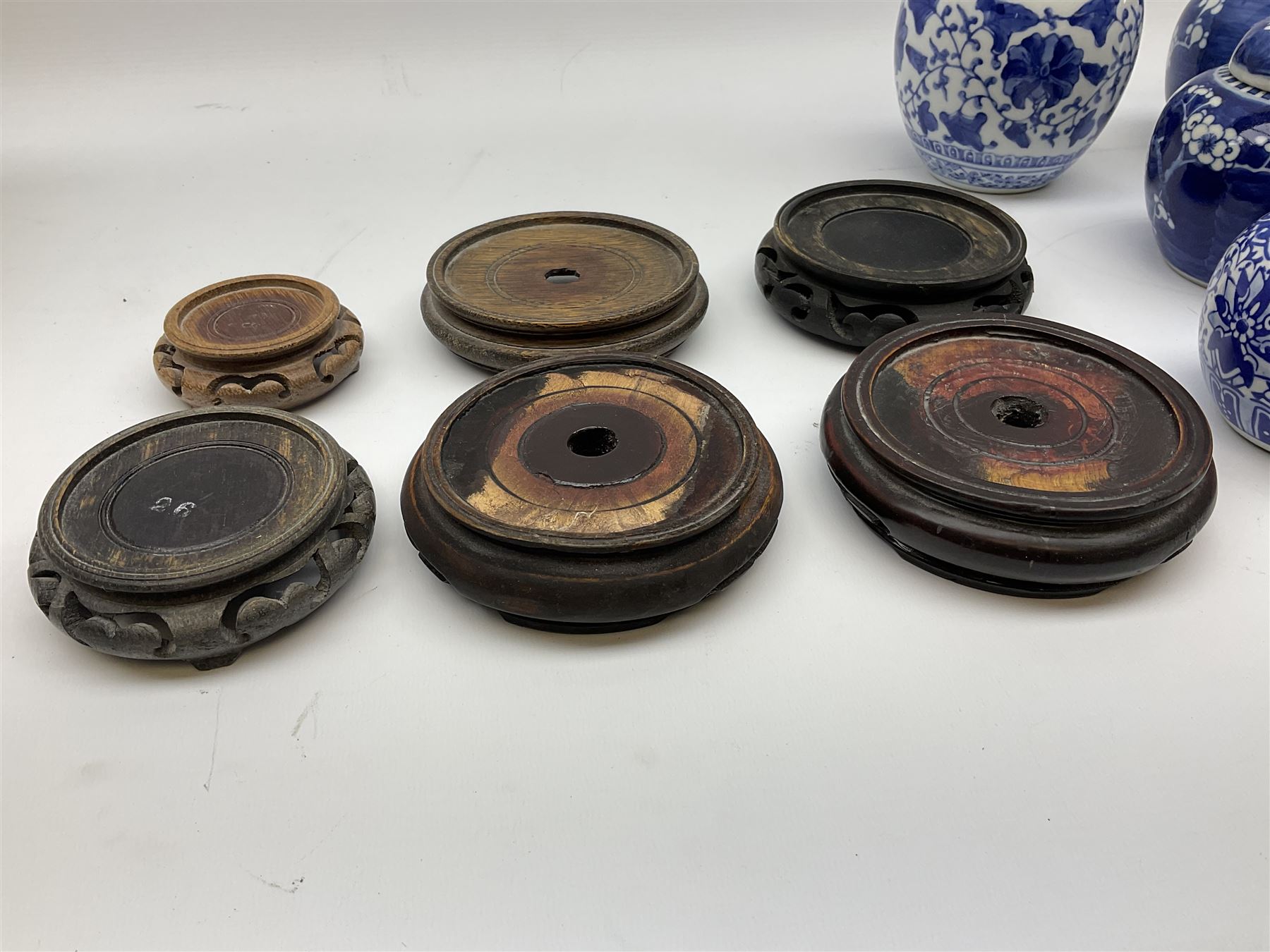 Six Chinese ginger jars, predominantly of blue and white design decorated with blossoming branches, all with lids, housed on various hardwood carved stands, some with character marks beneath