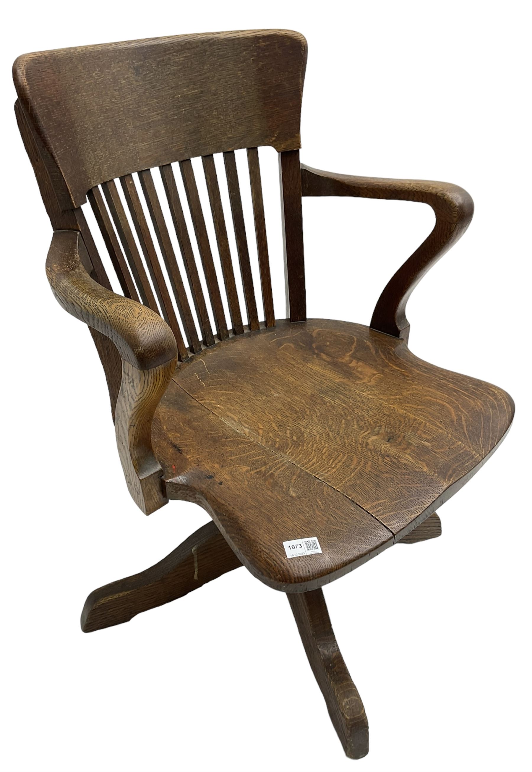 Early 20th century swivel office desk chair, shaped bar back over vertical rails, dished seat, on four splayed supports