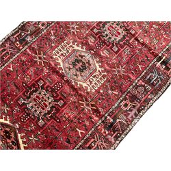 Persian Karajeh crimson ground runner rug, the field set with seven geometric lozenge medallions, the field decorated all over with stylised plant motifs, the banded border with repeating geometric shapes and patterns