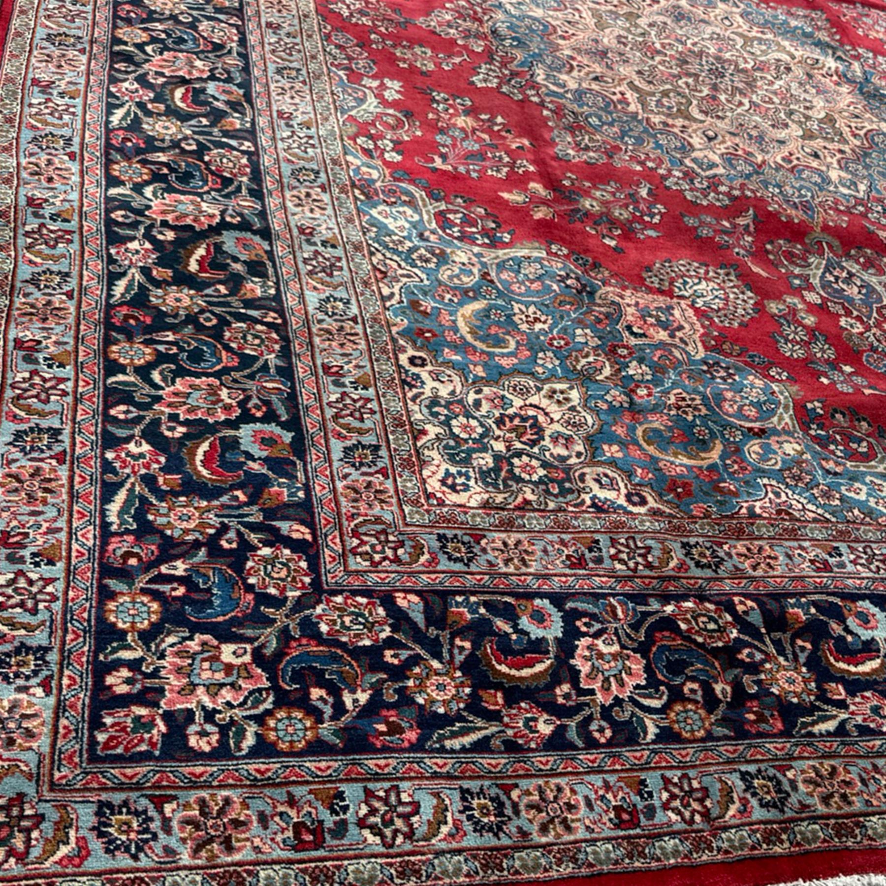 Meshed Persian rug, red, indigo, and teal background with repeating floral vine around a symmetrical floral medallion with bold palmettes, central ivory radiating floral centrepiece, and spandrels, indigo and teal border of delicate scrolling palmette and leafy floral vines
