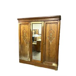 Late 19th century pitch pine triple wardrobe, shaped projecting cornice, central door with rectangular mirror plate, flanked by two panelled doors with floral foliate painted designs with trailing garlands, raised on plinth base, interior fitted with four sliding open shelves over four drawers