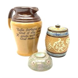Three pieces of Doulton Lambeth, comprising a motto ware jug, inscribed Take fortune as you find her and if she frown don't you. A smile will oft recall her and make her kind., H19.5cm, a tobacco jar and cover, and a dwarf candlestick, each with impressed marks beneath. 