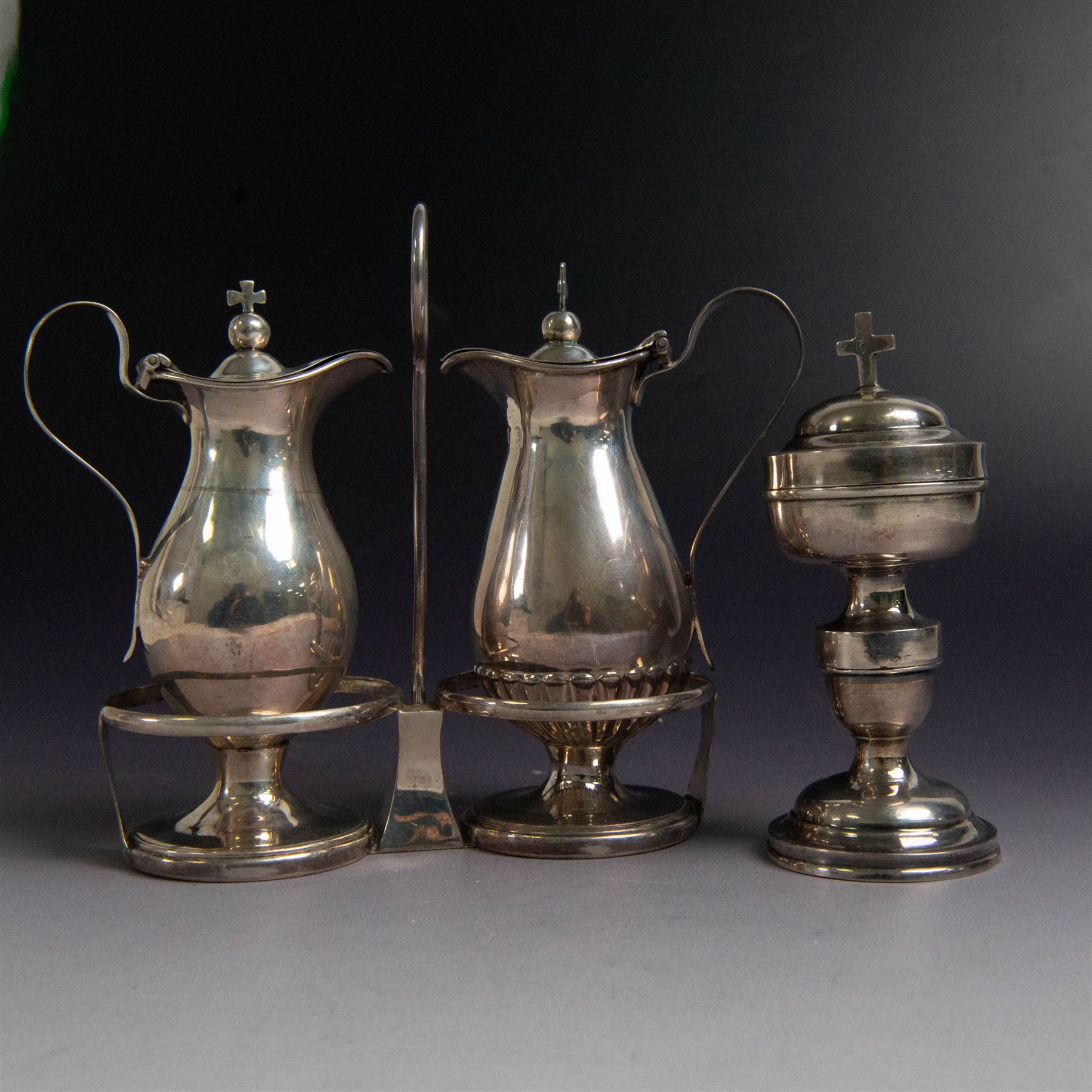 Ecclesiastical silver cruets, comprising two jugs in the form of miniature wine carafes, one hallmarked London 1825, the other unmarked, contained in a silver cruet stand with loop handle, hallmarked London 1937, and a French silver jar and cover in the form of a miniature chalice, with Minerva's head standard mark, tallest H13cm