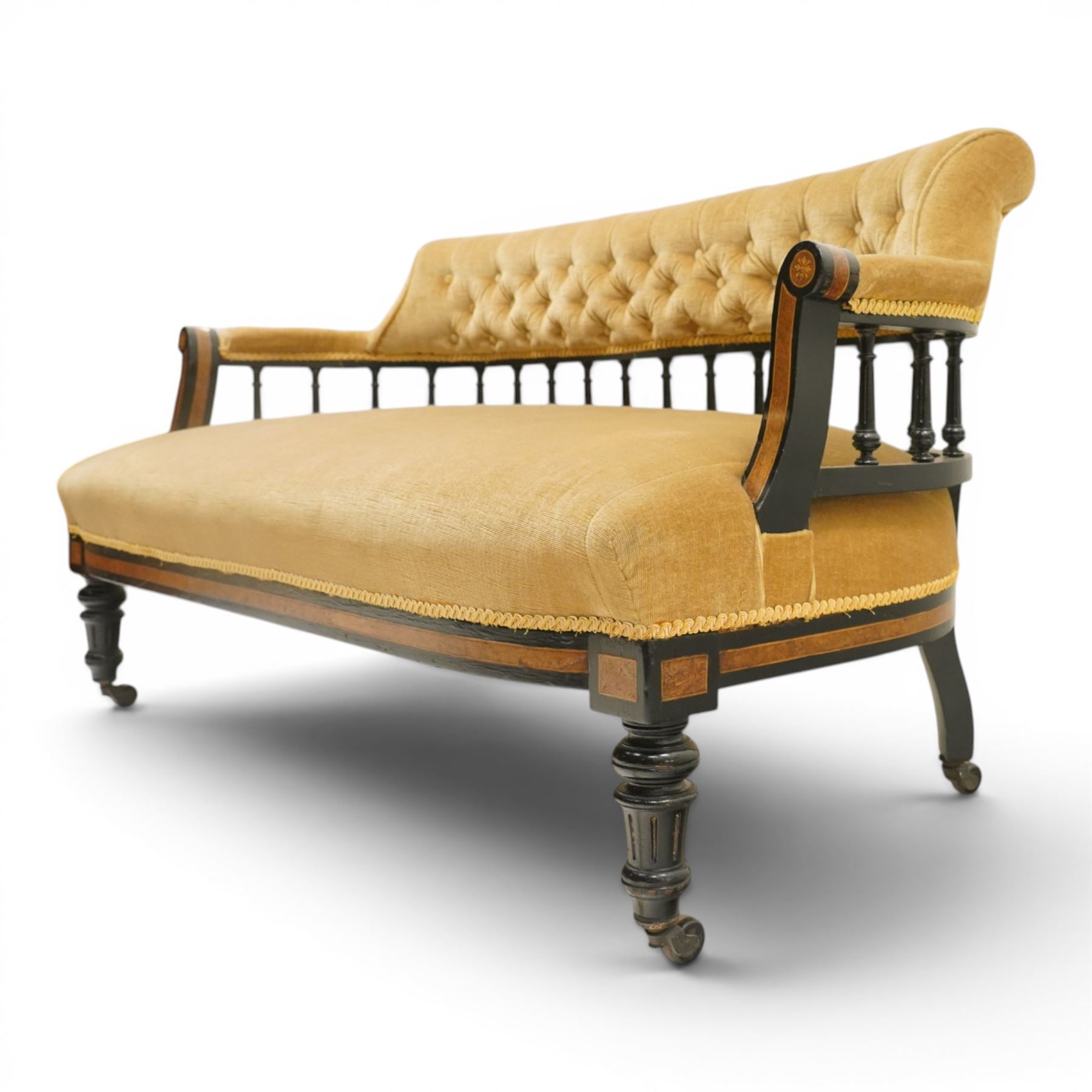 Late Victorian Aesthetic Movement settee, with buttoned upholstered roll-over back and arms, open spindle gallery frame with turned uprights, stuff-over seat, on shaped ebonised supports