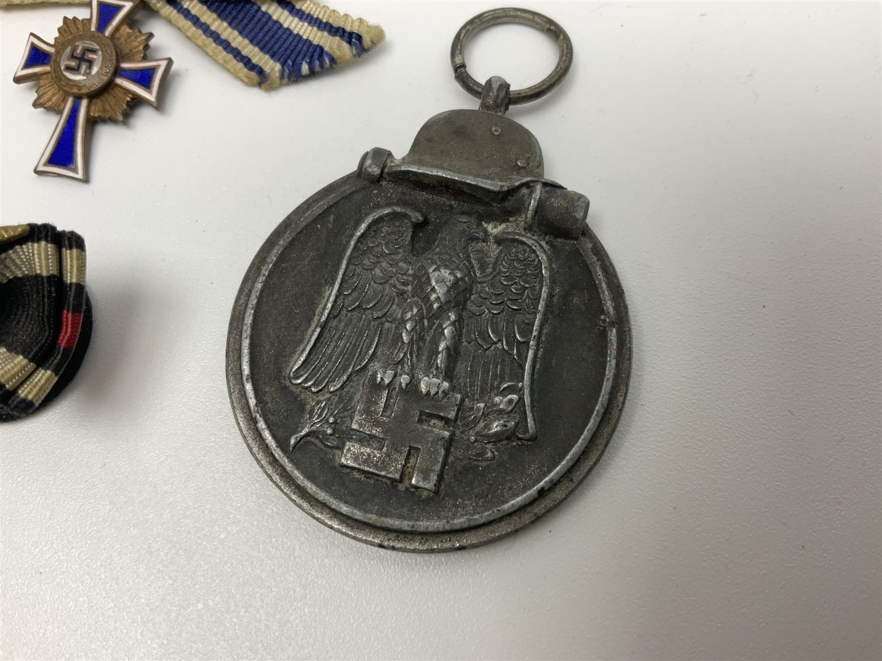 Four German awards - pre-WW2 two-position button hole ribbon for 1914 Iron Cross; WW1 wound badge open back cut-out version with silvered finish; miniature version Mother's Cross with ribbon bow; and The Eastern Medal, officially the Winter Battle in the East 1941–42 Medal (4)