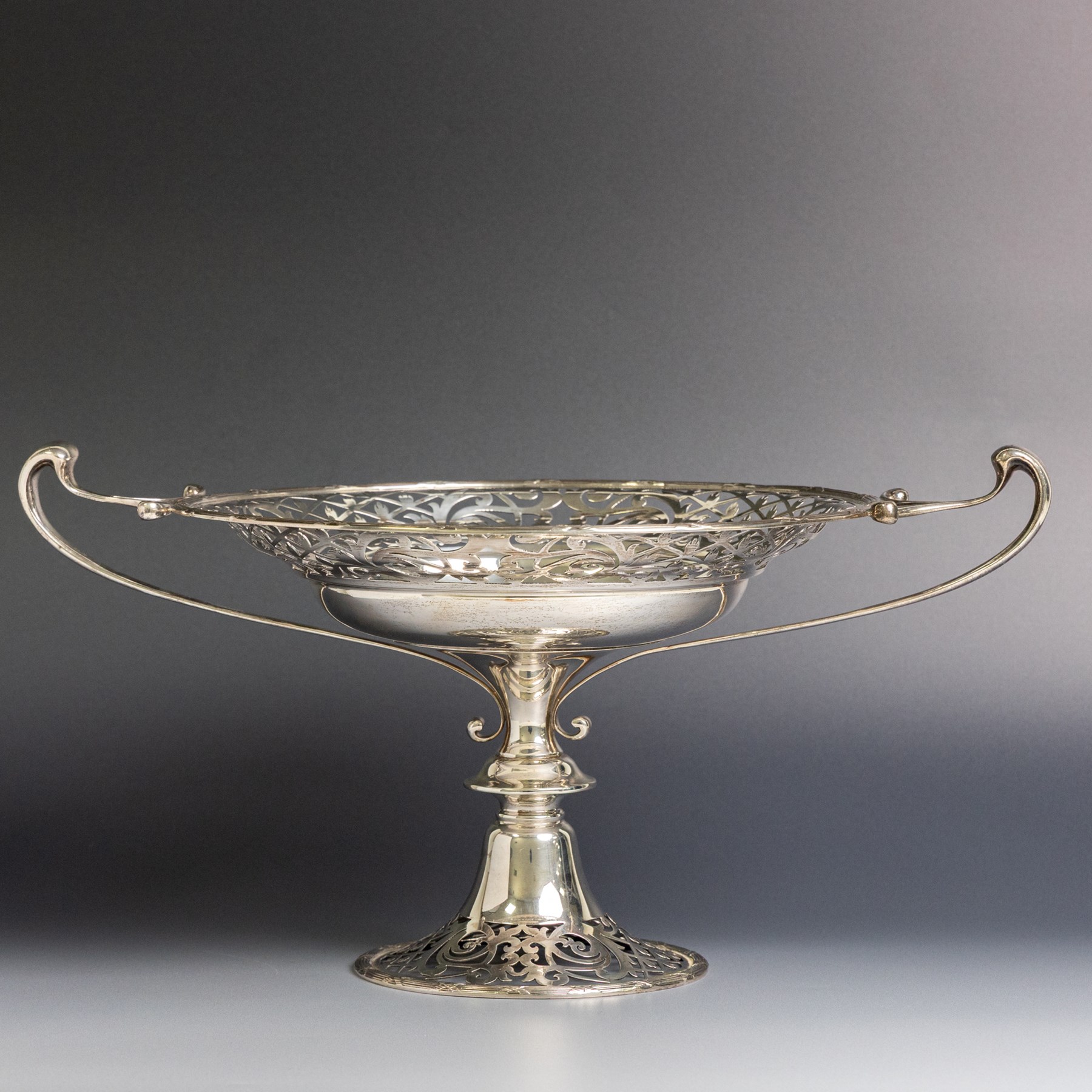 Early 20th century silver twin handled tazza, the bowl of circular form with pierced foliate decoration and ribbon and reed border, with two whiplash curved handles, upon a knopped stem and pieced foliate foot, hallmarked Walker & Hall, Sheffield 1911, H20cm