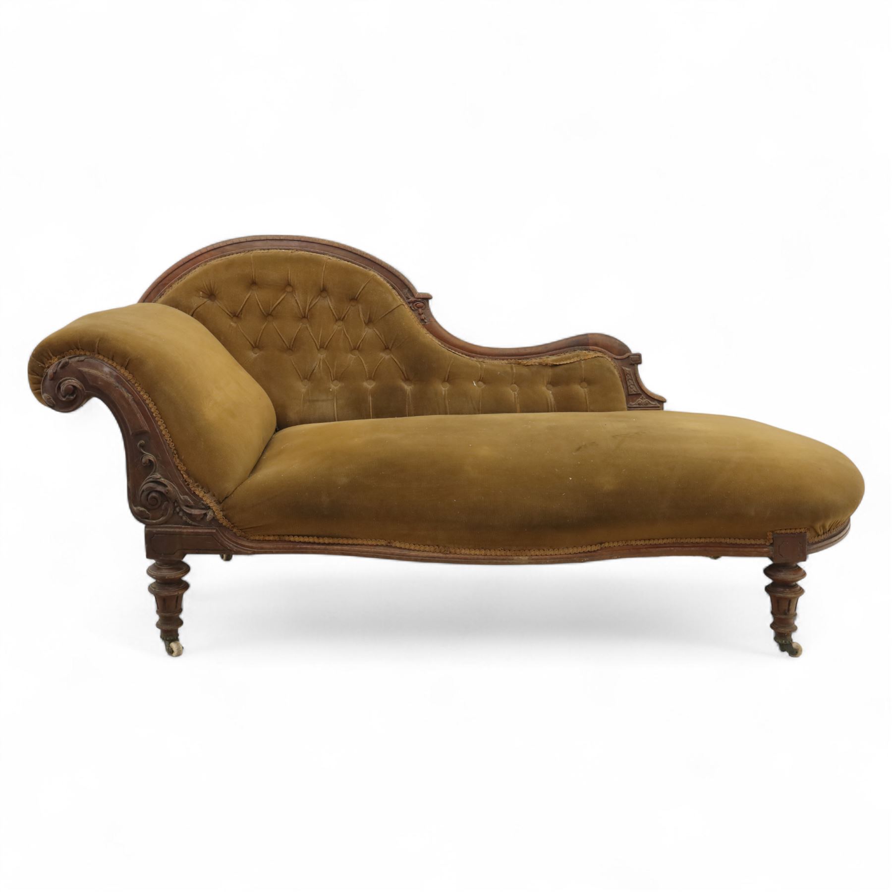 Victorian walnut framed Chaise longue, with carved scroll decoration and an out-swept buttoned upholstered, padded back and scroll end, seat upholstered mustard coloured velvet fabric, raised on turned legs with ceramic castors 