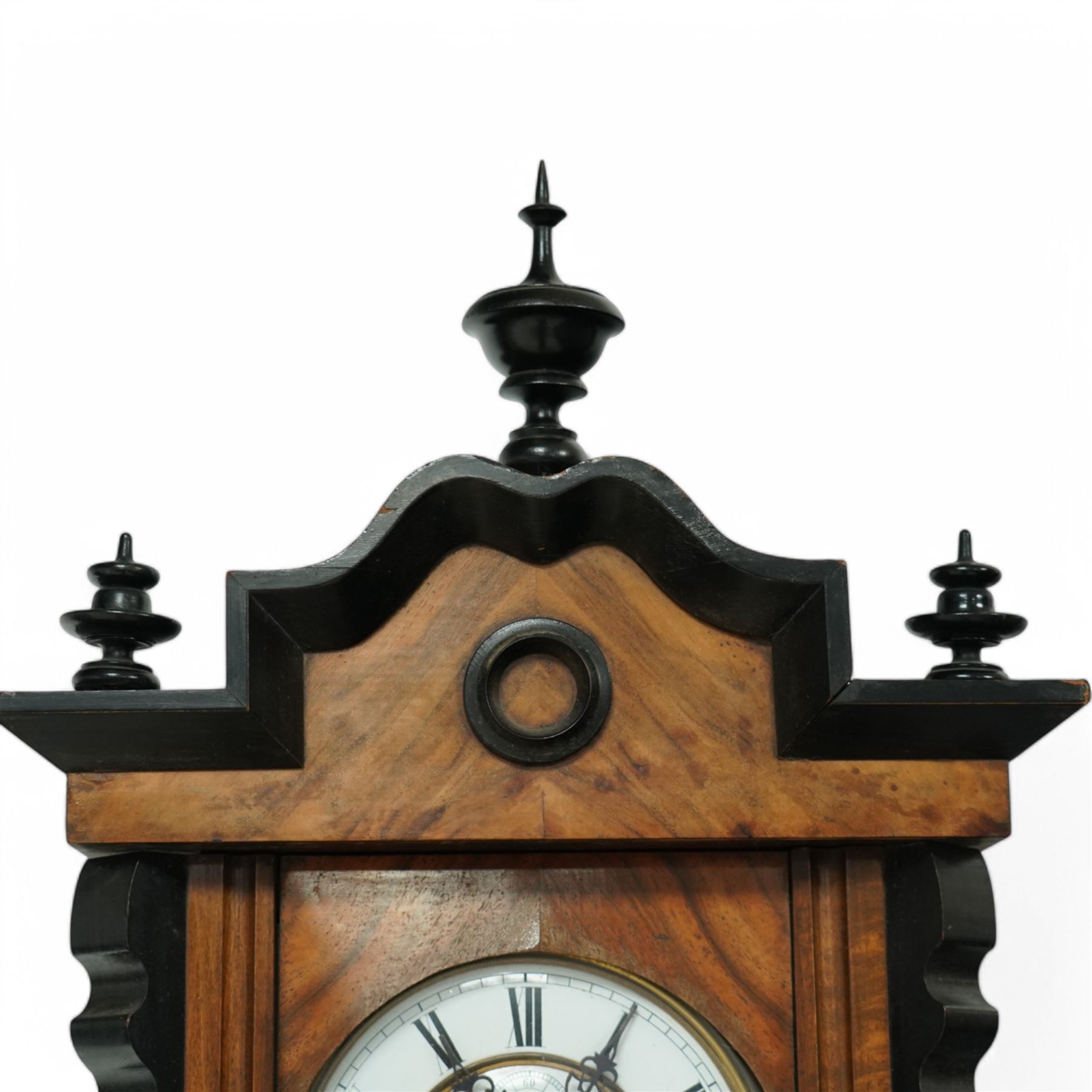 German- Late 19th century twin weight 8-day Vienna wall clock, in a walnut and ebonised case with turned finials and pendants, fully glazed door displaying the the brass cased weights and pendulum, enamel two-part dial with Roman numerals, minute rack, seconds hand and gothic steel hands, rack striking movement with a deadbeat escapement, striking the hours and half-hours on a coiled gong. With key.