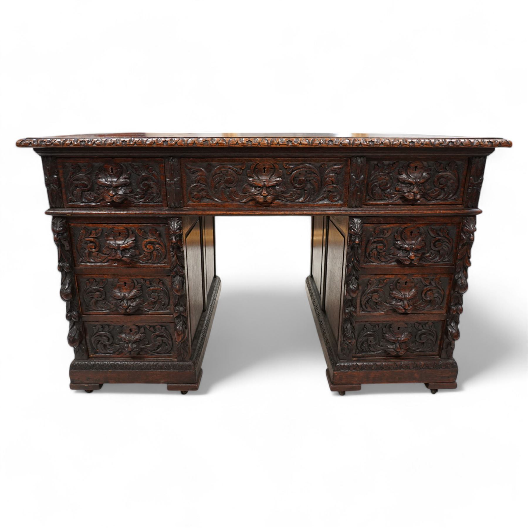 Victorian carved oak twin pedestal desk, moulded and foliate carved rectangular top with leather inset, fitted with nine drawers, each carved with scrolling foliage and lion mask handles, on skirted base 