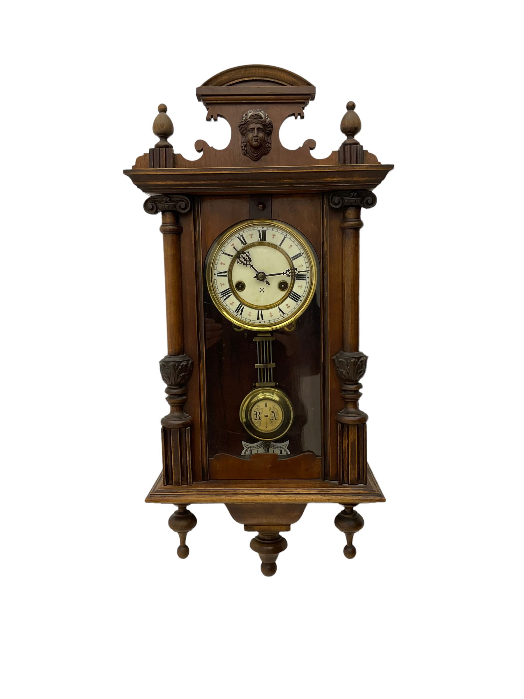 An early 20th century German wall clock with an 8-day HAC spring driven movement striking the hours on a coiled gong, in a mahogany case with a shaped pediment and turned columns flanking a full-length glazed door, with a two-part dial enamel with Roman numerals, minute track and pierced gothic designed hands, gridiron pendulum and beat plate. With Key.





