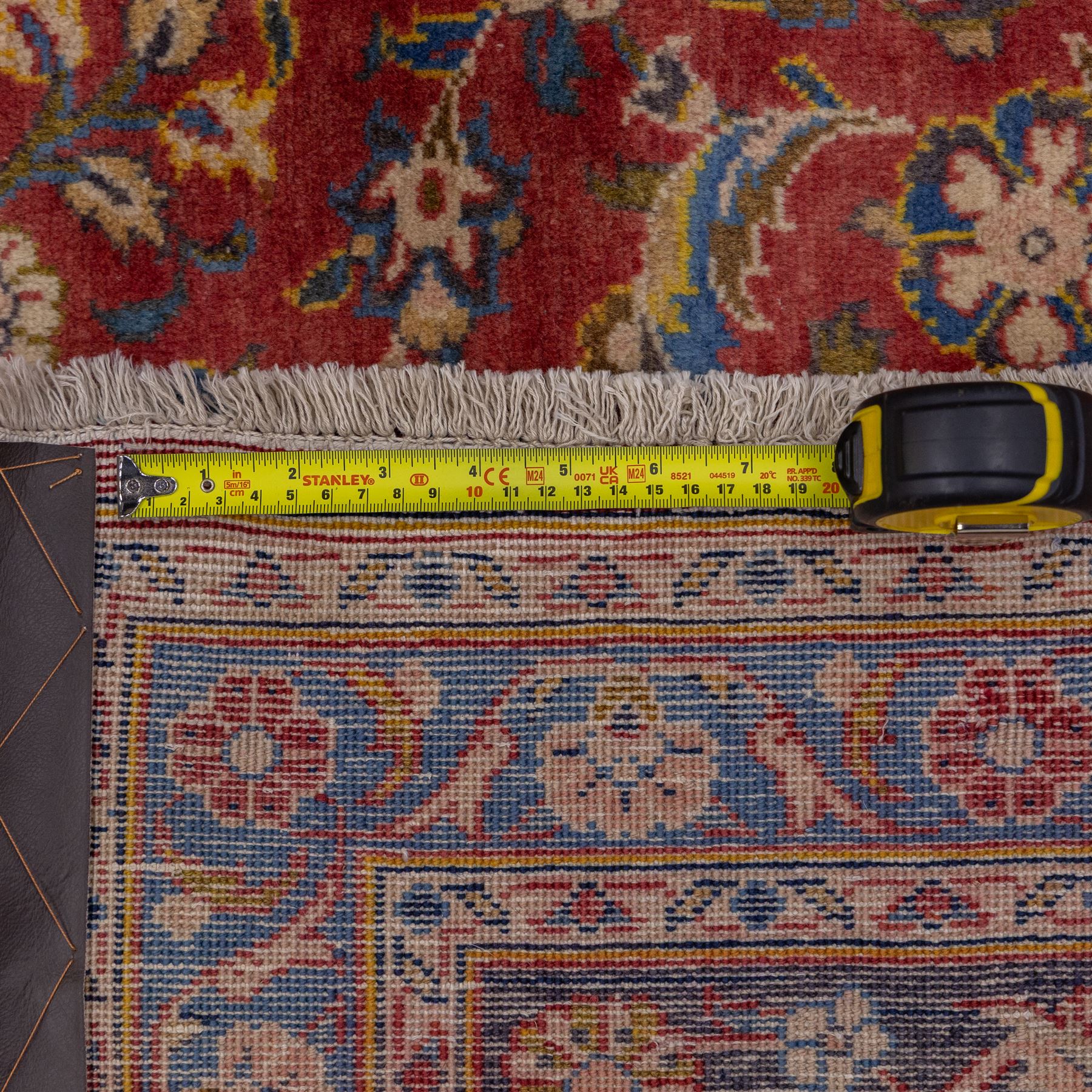 Central Persian Kashan hand-knotted carpet, madder red field with a central cusped medallion of ivory and deep indigo ground, enclosing a stylized floral rosette, framed by scrolling arabesques, field richly ornamented with an intricate network of flowering vinery, palmettes, and delicate floral sprays, spandrels in deep indigo, principal border of navy ground decorated with a continuous palmette and vine-scroll, flanked by multiple guard stripes, with cotton fringe ends 