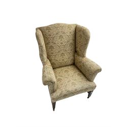 19th century wingback armchair, upholstered in ivory fabric with green and coral foliate pattern, scrolled arms with sprung seat, raised on mahogany tapering feet united by H stretcher, on brass castors 