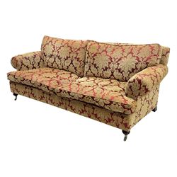 Duresta - pair of Grande three-seat sofas, traditional shaped with rolled arms and upholstered loose cushions, in red ground fabric with raised gold foliate pattern, on turned feet with brass castors 