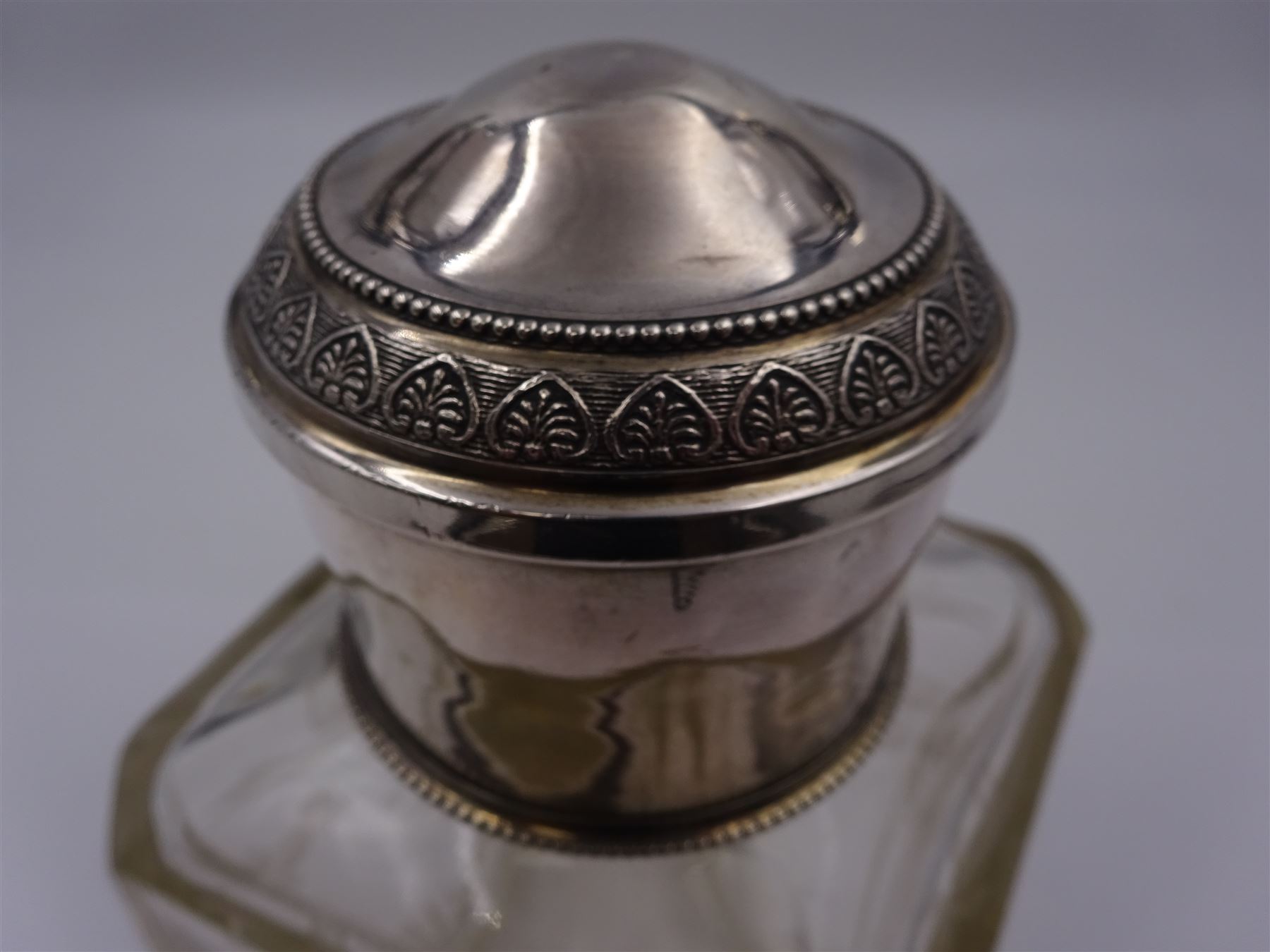 Early 20th century French silver mounted glass scent bottle, the faceted rectangular glass body etched with swags of flowers united by ribbons, with cylindrical silver cover embossed with foliate detail and beaded decoration with gilt interior, marked with Minerva's head, with white metal collar and glass stopper, H17cm