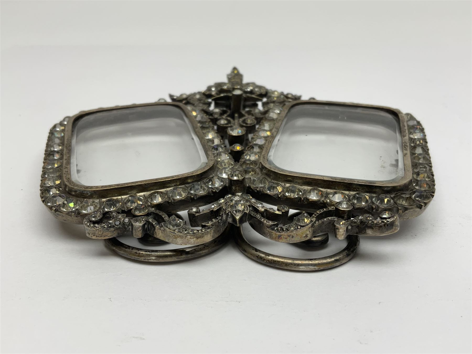 Early 19th century silver plated double photograph frame, each rounded rectangular aperture surrounded by a paste border, with ornate scroll feet and mantling also set with clear paste stones, with easel style support verso, H12cm