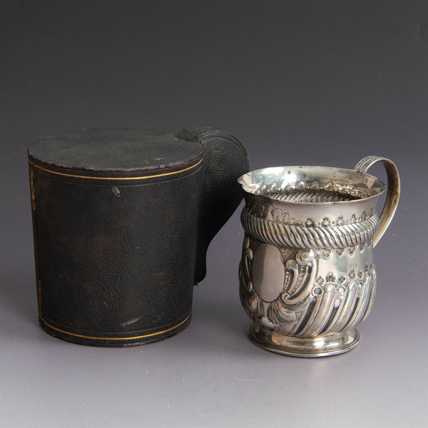 Victorian silver christening mug, of circular form with C scroll handle, embossed with scrolls and foliate decoration, with vacant oval cartouche to body, hallmarked John Aldwinckle & Thomas Slater, London 1890, contained within a tooled leather fitted case, mug H8cm