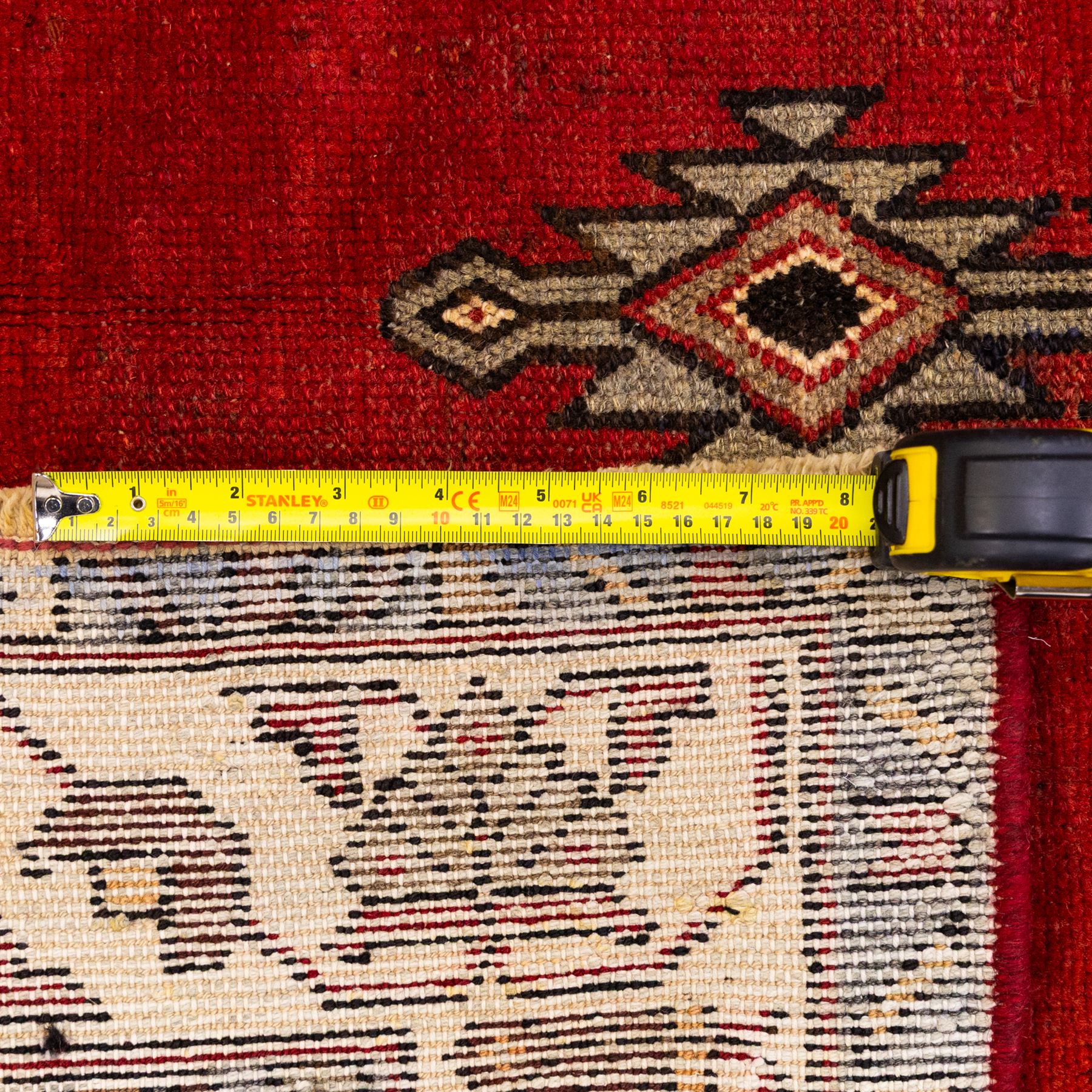 West Persian Mazlaghan hand-knotted rug, madder red field with central stepped lozenge medallion with pendant motifs flanked by angular serrated spandrels filled with small geometric devices, enclosed within multiple borders featuring stylized floral and geometric motifs, with cotton fringe ends 