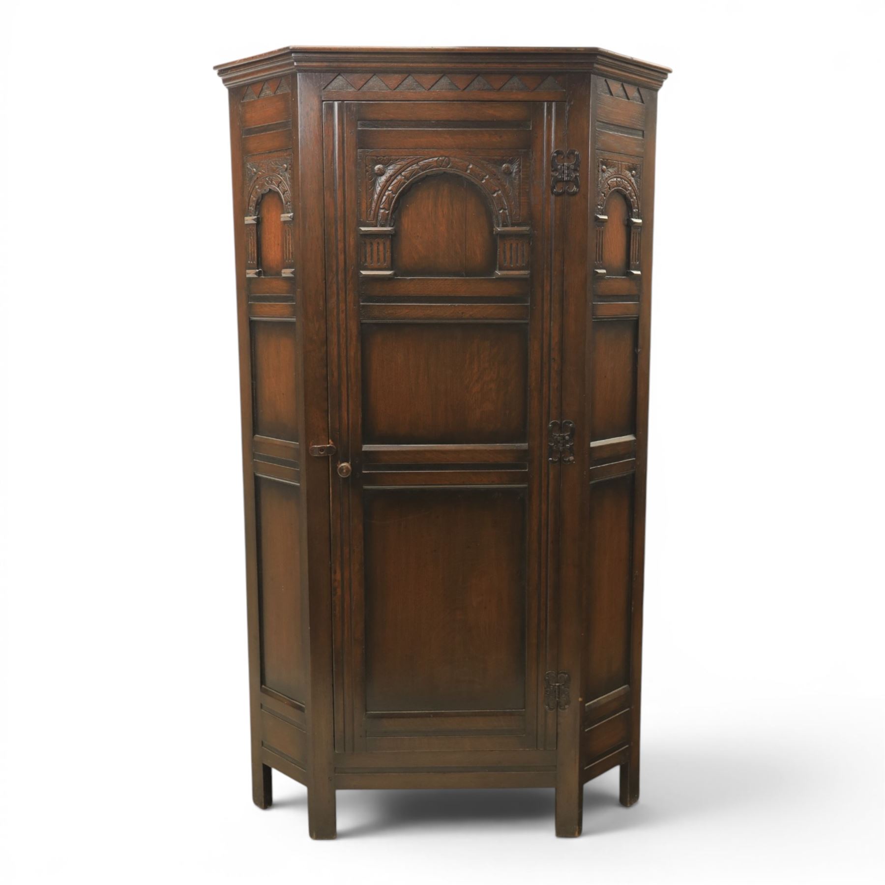 20th century dark stained oak hall robe, cantered sides enclosing a hooks and a shelf, panelled and carved sides, raised on stile supports