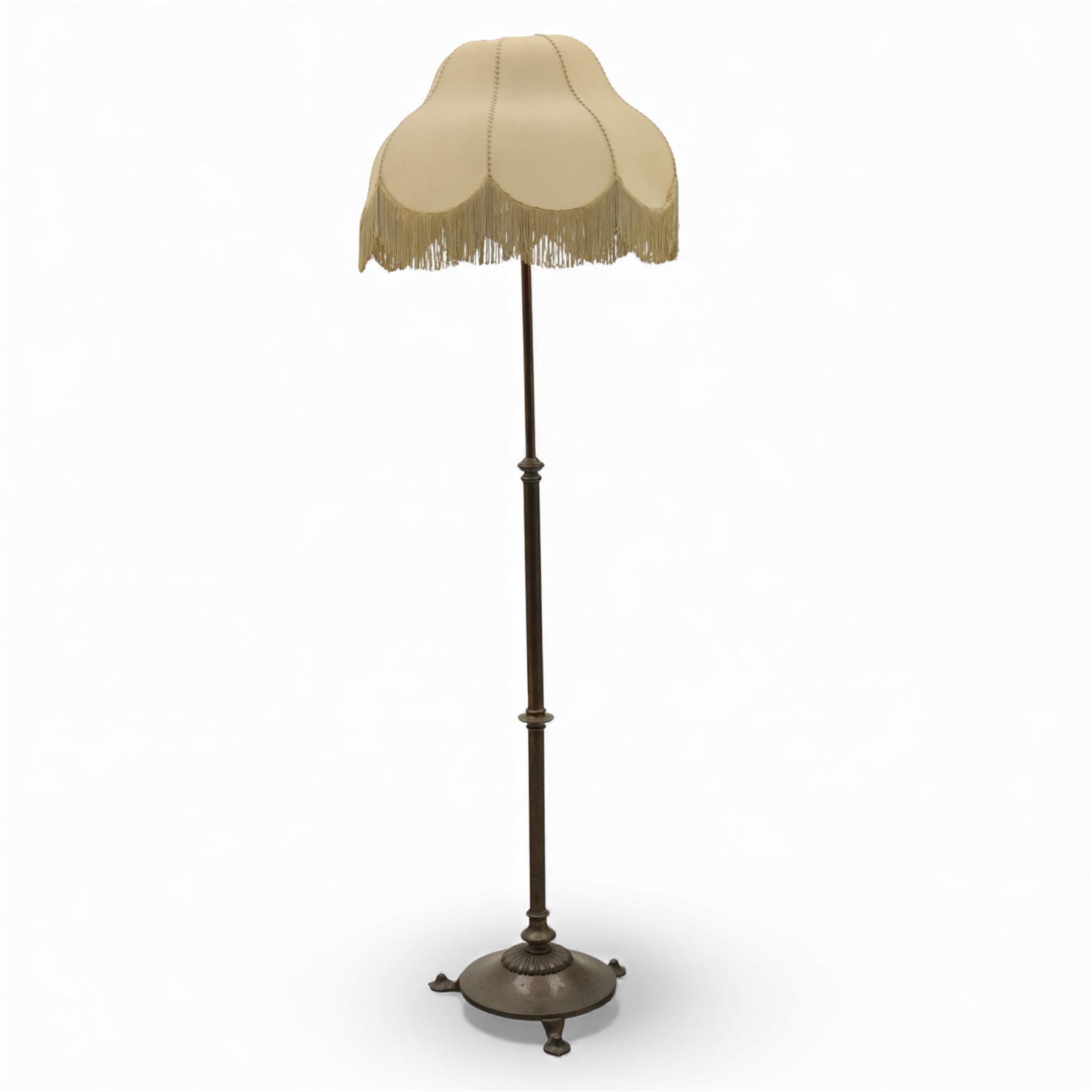 Early 20th century Art Nouveau metal standard lamp, the slender column with adjustable collar, raised on a circular dished base with three pad feet, fitted with a metal gallery and bulb holder, beige raw hide with fringe 