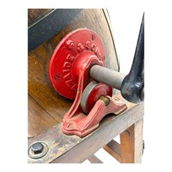 19th century oak and cast iron rotary butter churn, with coopered barrel body, domed lid with filler opening and cast iron securing arms, on tilting iron-mounted frame with crank handle and support rails