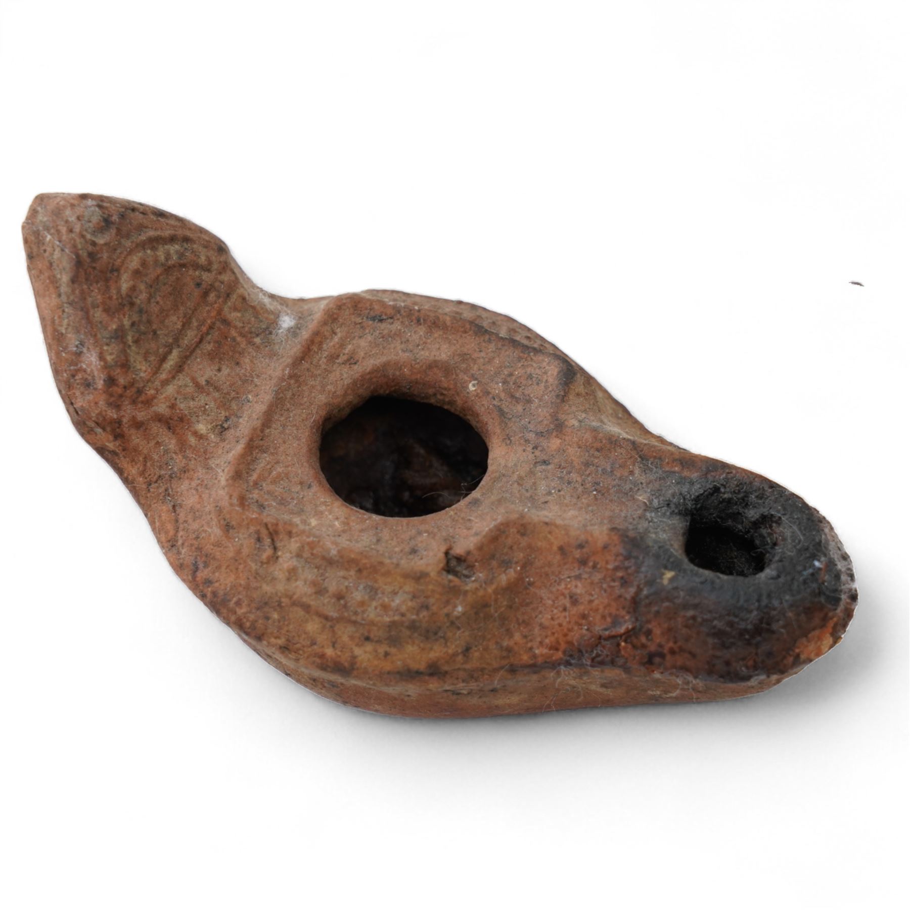 A group of four Byzantine terracotta oil lamps - Eastern Mediterranean, c.5th-7th century AD, comprising a group of mould-made slipper-form oil lamps, each with a rounded body, large central filling hole, and a short to elongated nozzle; including one with fine radiating linear decoration, and another preserving ancient use with traces of oil and wick residue within the burnished interior; together with a Crusader-period terracotta oil lamp (c.12th-13th century AD) of angular form with recessed panel decoration and a pierced handle moulded as a stylised animal head
Provenance: By the vendor’s repute, acquired/collected in the Middle East (Dead Sea area/Syria) in the 1960s