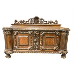 Late 19th century heavily carved walnut sideboard, raised back with pierced and carved fleur-de-lis with extending scroll and foliate decoration, moulded and carved edge with repeating cartouche design, central panel with fruit motifs flanked by two cupboards, the edge reeded cluster columns with acanthus leaf capitals, raised on large clawed feet