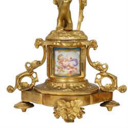 Pair of 19th century ormolu putto figures, each modelled stood with foliate support to backs, upon a naturalistic base upon cylindrical plinth each with twin leafy tendril supports, each plinth with inset Sevres type painted panel of a cherub, upon a shaped base with four compressed disk feet, the front facing with leaf mount, H29cm